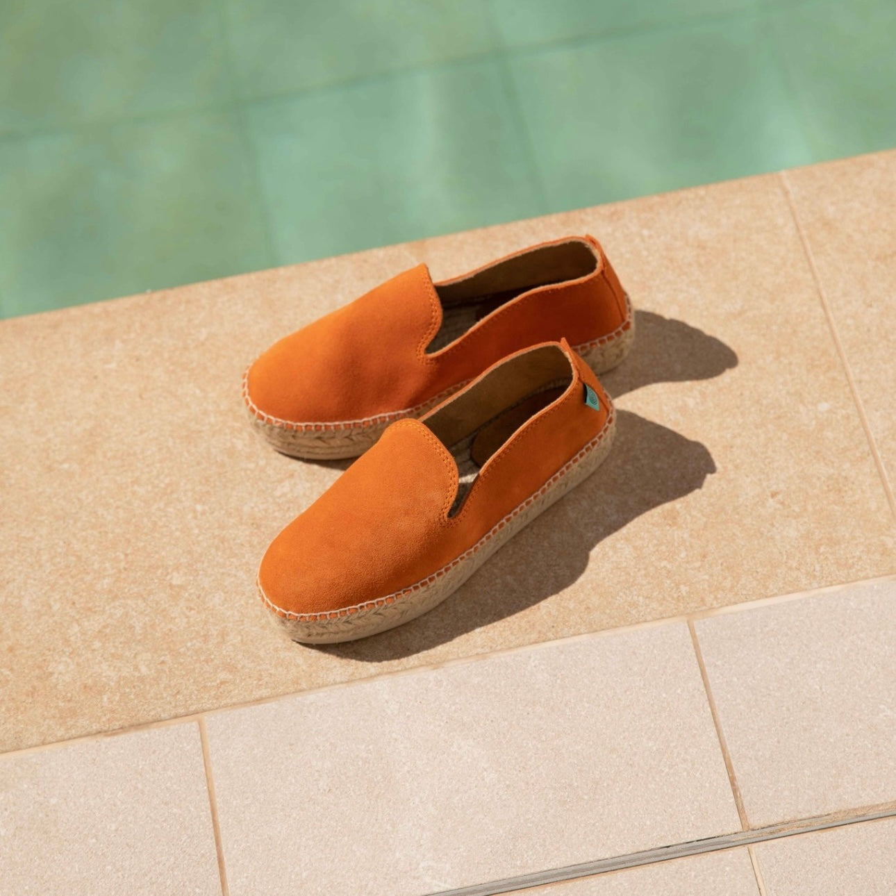 Orange velour leather espadrille shoes sitting next to a pool